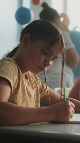 Elementary School Students Writing Exam or Doing Tasks in Notebooks. Female Teacher Walking Between Desks, Controlling Young Boys and Girls During School Test in Classroom. Dolly Shot. Vertical Shot.
