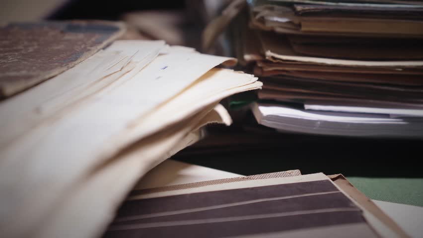 Untidy piles of historical documents on moody lit research desk scene