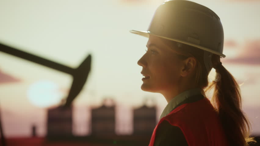 Engineers collaborating in safety gear, discussing petroleum operations at golden hour sunset near oil pump and industrial equipment