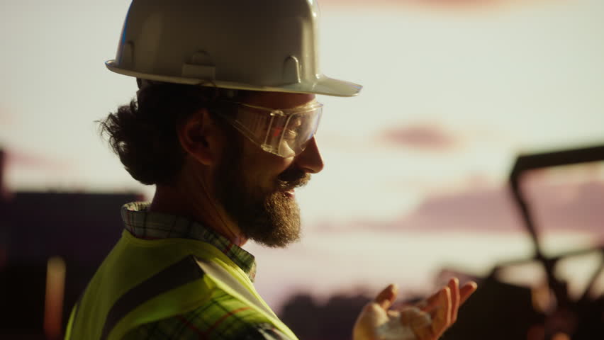 Professional engineers collaborating during sunset, wearing safety gear near oil pump, analyzing industrial project in expansive petroleum field