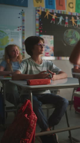Elementary School Students Sitting at the Desks, Listening to Lecture, Raising Hands to Provide Correct Answer. Team of Smart Diverse Kids Studying Science, Geography in Classroom. Vertical Shot.