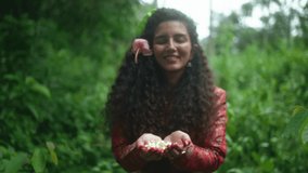 Smiling South Asian woman with long curly hair and red traditional dress offers jasmine buds in a forest setting, evoking a Jal Arpan-inspired nature ritual of gratitude and purification. - Powered by Shutterstock - Get 15% off with code: PIKWIZARD15