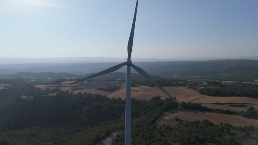 Two wind turbines are rotating against a clear blue sky, harnessing wind power to generate sustainable and clean energy, symbolizing renewable energy and environmental conservation