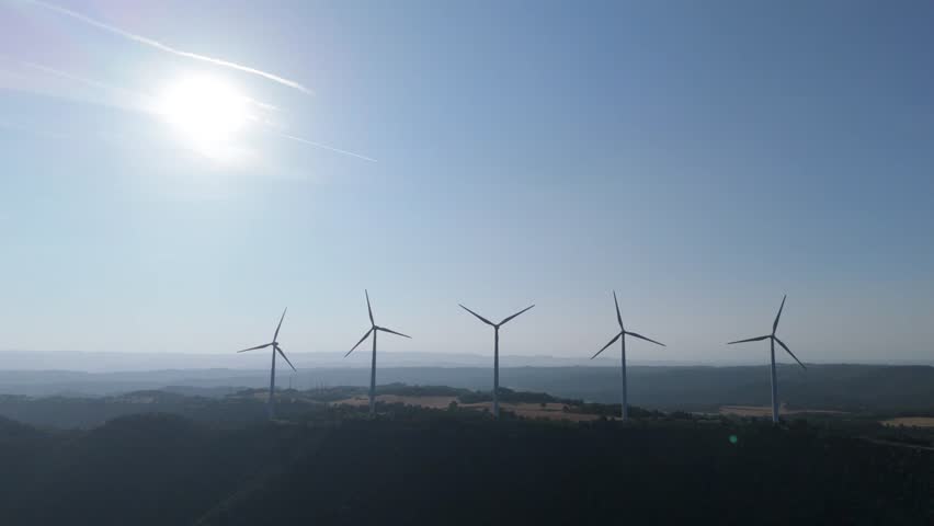 Two wind turbines are rotating against a clear blue sky, harnessing wind power to generate sustainable and clean energy, symbolizing renewable energy and environmental conservation