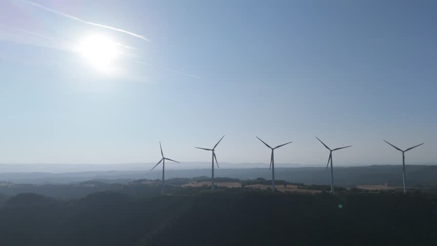 Two wind turbines are rotating against a clear blue sky, harnessing wind power to generate sustainable and clean energy, symbolizing renewable energy and environmental conservation