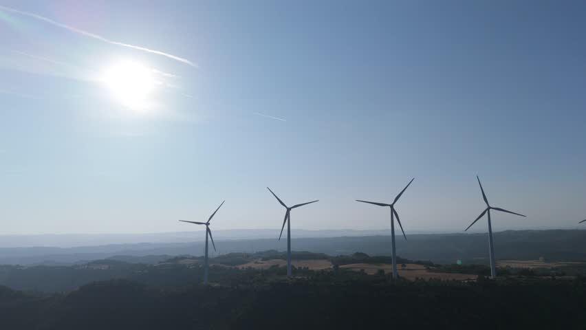 Two wind turbines are rotating against a clear blue sky, harnessing wind power to generate sustainable and clean energy, symbolizing renewable energy and environmental conservation