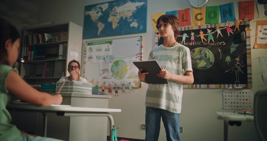 Renewable Energy Lesson: Elementary School Boy Holding Notebook Speaking, Giving Presentation on Geography in Front of Classmates and Teacher. Student Showcasing Knowledge of Ecology. Dolly Shot.