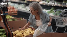 An elderly senior woman carefully selects bananas while grocery shopping in a vibrant store full of fresh fruits and vegetables, enjoying the variety available. - Powered by Shutterstock - Get 15% off with code: PIKWIZARD15