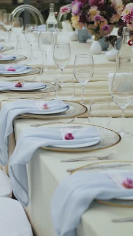 Vertical video. Beautifully decorated wedding table with pink flowers at a wedding or event, with plates and glasses. White chairs near the festive table. Flower arrangement on the table, slow motion.