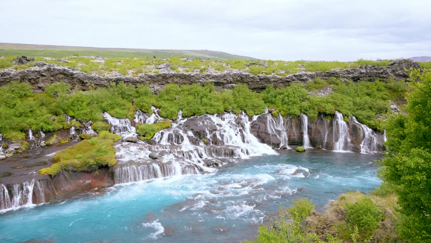 Footage of Hraunfossar Waterfall, with white cascades meeting turquoise river waters in West Iceland during summer. A truly unique natural wonder.