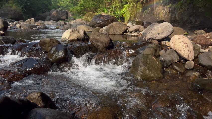 A calm river current creates pearl-like foam among the rocks. 4K 30 FPS.