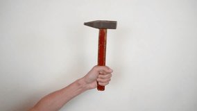 Close-up of a hand holding a hammer with a wooden handle and a metal striker against a light wall. The hammer is raised up, as if ready to work. - Powered by Shutterstock - Get 15% off with code: PIKWIZARD15