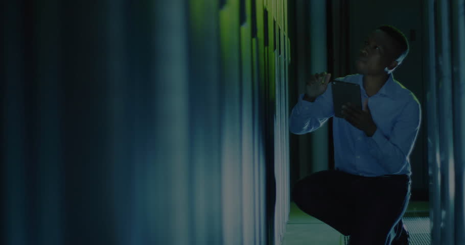 Technician kneeling in data center inspecting racks causing colored line graphs monitoring metrics. Technology, data analysis, cybersecurity, digital infrastructure, real-time monitoring, networking,