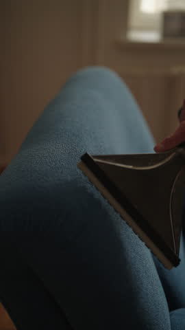 Close-up vertical cropped shot of homemaker vacuuming dirty couch with upholstery attachment, removing dust and debris with careful, thorough technique for deep fabric cleaning, close-up, slow motion.
