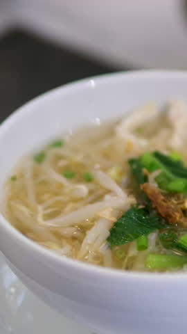 A steaming bowl of Pho, a traditional Vietnamese noodle soup, garnished with fresh herbs, chili peppers, and beef meatballs. The appetizing broth and vibrant ingredients create a delicious visual.