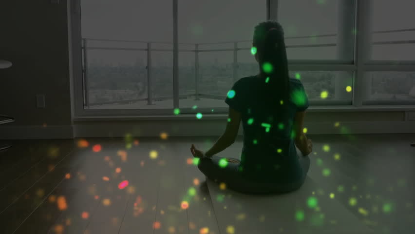 Woman sitting cross-legged by window, breathing and generating health particles shifting green. Mindfulness, serenity, meditation, wellness, tranquility, zen, spirituality