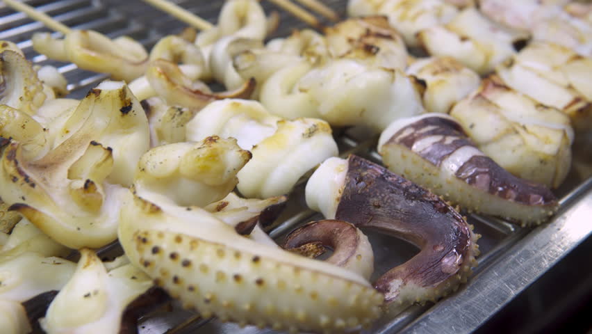 Octopus satay and squid satay (sate) at a night food market in a Chinatown. Grilled seafood is a popular tourist street food in Asia.