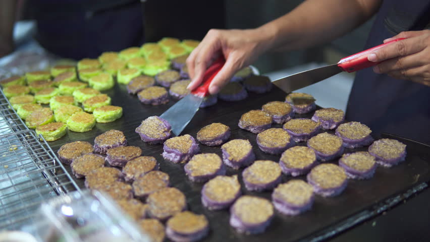 A vendor prepares colorful Thai traditional cakes on a hot griddle at Night Market of Chinatown, Bangkok.
