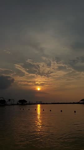Sunset on an Indonesian beach. A large sun in the twilight sky touches the horizon. The Java Sea is in the background. Sunlight trails on the water. A stunning orange sunset at sea.