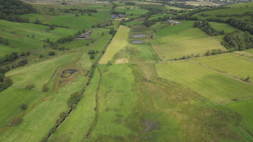 Aerial view of green farmland with scattered ponds and farmhouses in the distance.
