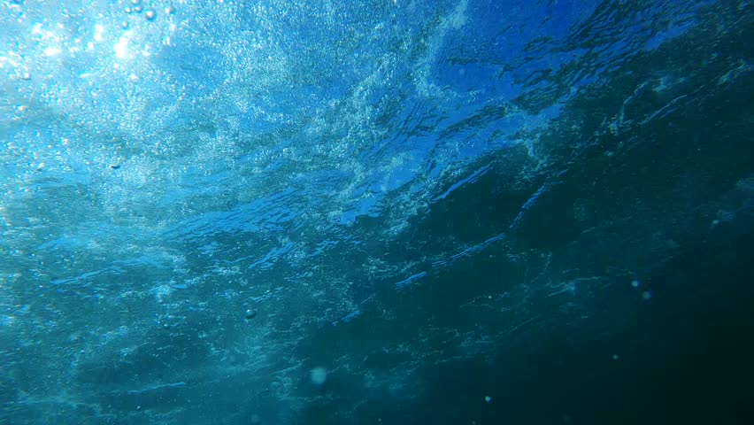 Underwater view filled with air bubbles and sunlight streaming through the surface, capturing the dynamic beauty of the ocean depths. 4K, low angle view.