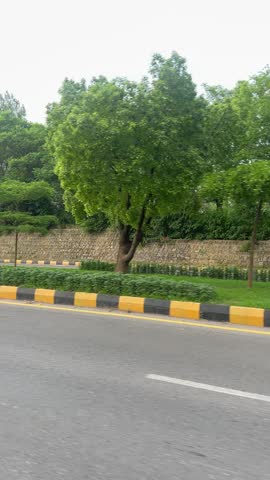 Wide road in Islamabad heading towards Faisal Mosque, with light traffic, green trees, and Margalla Hills in the distance. Ideal for city, travel, and Pakistan-themed concepts.