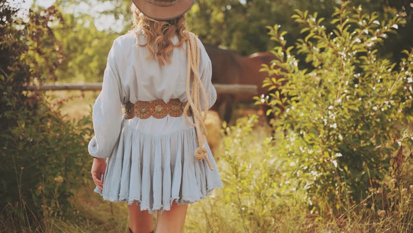 Happy Woman cowgirl with horse holds lasso rope back rear view. bale of hay dry grass straw field nature summer. lady ranch owner in leather hat belt. sexy Girl short dress country style wild west 4k
