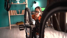 Young woman in eyeglasses and orange shirt repairing bicycle at home. Bike repair and maintenance - Powered by Shutterstock - Get 15% off with code: PIKWIZARD15