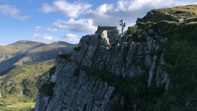 Male hiker standing on top of a rocky cliff in the mountains with trekking poles, looking at the scenic mountain landscape under a cloudy sky - Powered by Shutterstock - Get 15% off with code: PIKWIZARD15