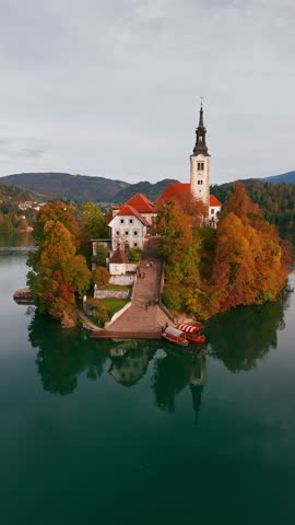 Aerial view of majestic Lake Bled at sunrise in autumn, Slovenia. Close-up of the Pilgrimage Church on the island, Bled Castle on a cliff, and a hot air balloon floating above the picturesque lake.