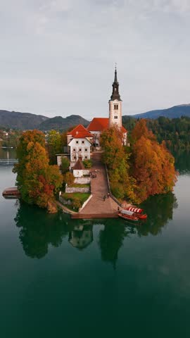Aerial view of majestic Lake Bled at sunrise in autumn, Slovenia. Close-up of the Pilgrimage Church on the island, Bled Castle on a cliff, and a hot air balloon floating above the picturesque lake.