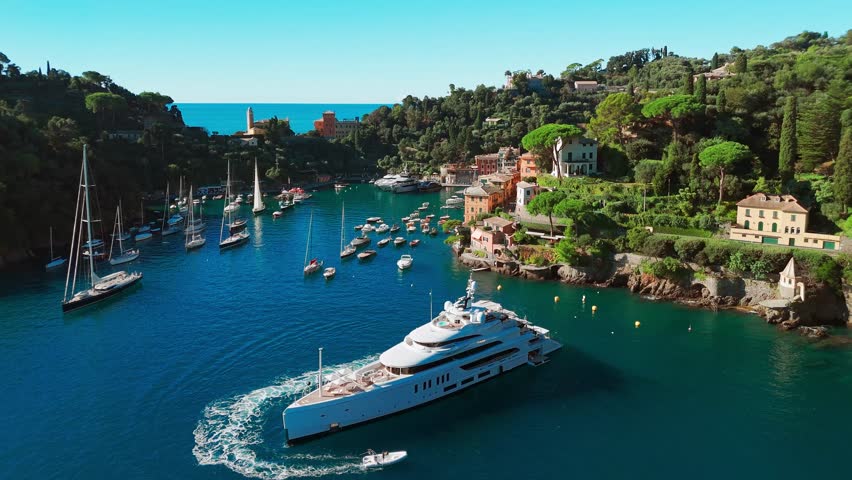 Aerial view of the picturesque resort town of Portofino in Liguria, Italy. Charming harbour with moored sailboats and luxury yachts surrounded by historic colorful buildings along the Ligurian coast.