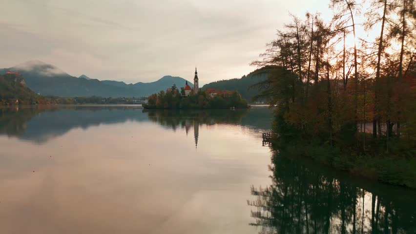 Aerial view of Lake Bled at sunrise in autumn, Slovenia. Scenic landscape with Pilgrimage Church on the island and medieval Bled Castle on a cliff above the picturesque lake surrounded by mountains.