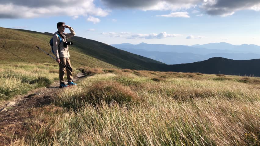 Man hiking on alpine trail with trekking poles under clear blue sky. Solo mountain adventure and outdoor exploration