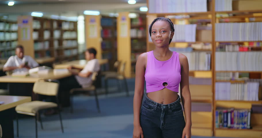 African young adult gen z happy beautiful student standing at library look camera show two hand thumbs up sign ready for exam. Smiling teenager girl staring cam do pose enjoy day time inside college