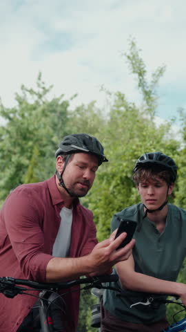 Father and teenage son checking bike route on smartphone during cycling trip.