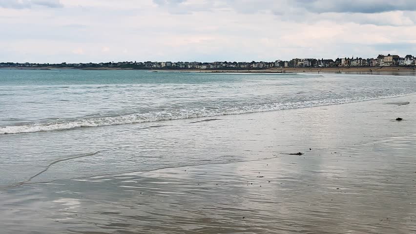 Mirror-like surface of wet sand and small waves at low tide in the English Channel on a Plage de l’Eventail beach overlooking the Intra-Muros district of Saint-Malo, Brittany, France.