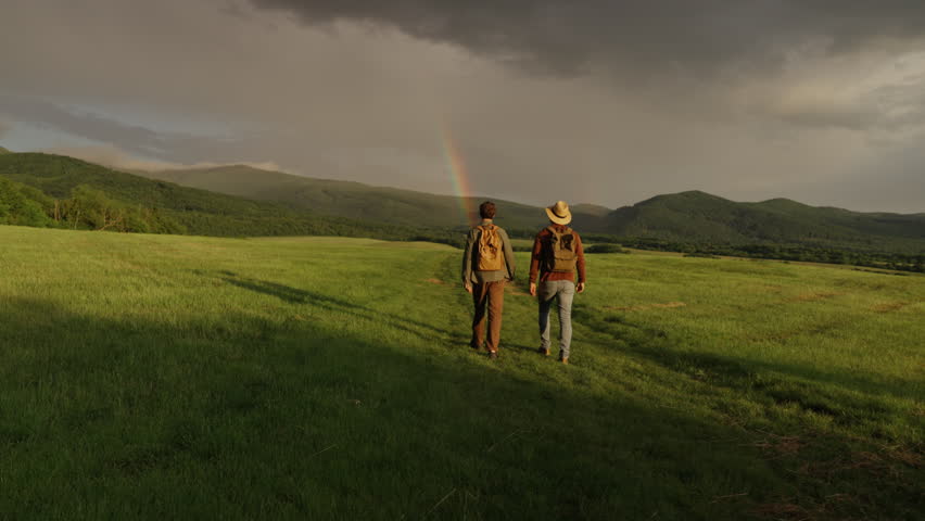 Father and son hiking together and watching a distant storm with a rainbow on the horizon.