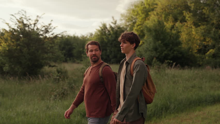 Dad and son walking through nature on hiking trail.