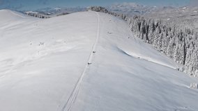 Two snowmobiles driving up a snowy mountain slope, leaving tracks in fresh snow, on a sunny day with clear blue sky and snowy forest on the side. Bukovel ski resort. Winter nature travel background - Powered by Shutterstock - Get 15% off with code: PIKWIZARD15