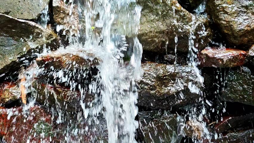 A focused close-up of splashing waterfall hitting layered rocks, showcasing dynamic water impact and natural texture in vibrant daylight.