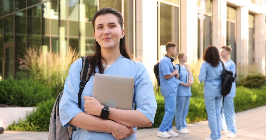 Medical student with laptop checking time near building outdoors, selective focus
