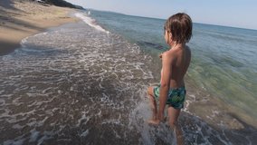 Slow motion video of a boy running through shallow waves on a sunny beach, water splashing around his feet, joyful summer moment in nature - Powered by Shutterstock - Get 15% off with code: PIKWIZARD15