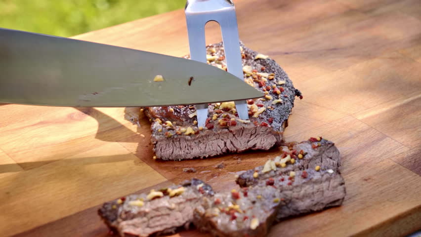 Close-up of a chef cutting a steak on a wooden cutting board.