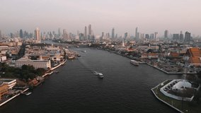 Aerial view of ferry gliding across chao phraya river, Bangkon, Thailand, urban skyline during golden evening light with sweeping architectural landscape - Powered by Shutterstock - Get 15% off with code: PIKWIZARD15