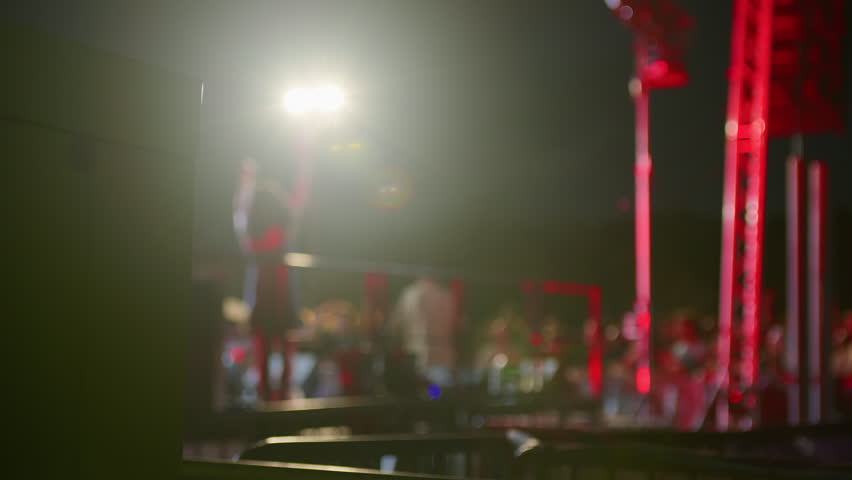 Shot behind stage showing blurred artist and cheering crowd. Captures dynamic energy and scale of live music event from unique backstage perspective. Perfect for concert promos.