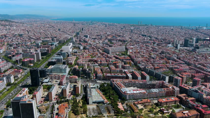 Wide drone view of Barcelona as Avinguda Diagonal leads across the Eixample grid to the Mediterranean coast. Sunny cityscape for travel, urban planning and real estate stories.