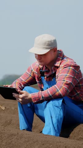CHERKASY, UKRAINE, APRIL 28, 2020: farmer, agronomist sits between special soil rows on field. he tests, using tablet, quality of potatoe planting by cultivator. Modern Agriculturally potato cultivati