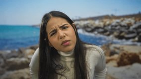 Woman tilts head and reveals face with squinting eyes on a beach emphasizing latin hispanic features in an outdoors seaside setting as a young model conveys expression. - Powered by Shutterstock - Get 15% off with code: PIKWIZARD15