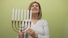Woman holds a brass nine-branch menorah with bare hands in a light green studio setting; holiday tradition faith joy. - Powered by Shutterstock - Get 15% off with code: PIKWIZARD15